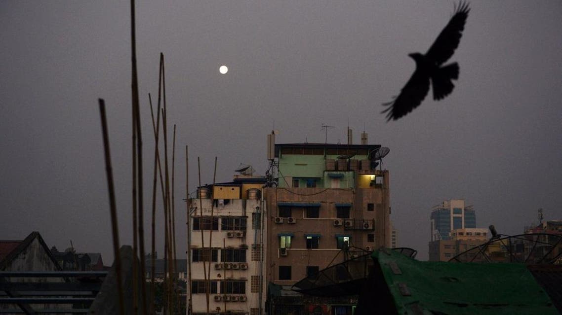 A crow flies over rows of residential apartments as the full moon descends at dawn over Yangon on February 24, 2016. AFP PHOTO / ROMEO GACAD