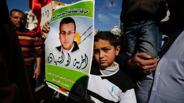 Palestinians hold placards depicting a portrait of journalist Mohammed al-Qiq imprisoned by Israel, as they celebrate the announcement to end his 94-day hunger strike under a deal for his release in May. (AFP)