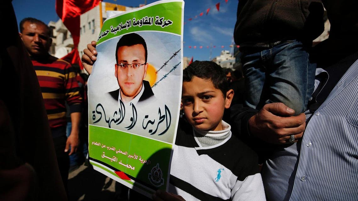 Palestinians hold placards depicting a portrait of journalist Mohammed al-Qiq imprisoned by Israel, as they celebrate the announcement to end his 94-day hunger strike under a deal for his release in May. (AFP)