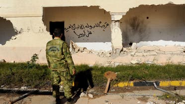 In this picture taken Wednesday, Feb. 24, 2016, A Libyan army soldier looks at damages with Arabic that reads, "soon, the Islamic State will be in Libya," in Benghazi. AP