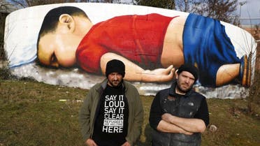   Artists Justus Becker (R) and Oguz Sen stand in front of a huge graffiti artwork of Syrian toddler Aylan Kurdi, after finishing a three-day painting session on a wall on the banks of river Main near the headquarters of the European Central Bank in Frankfurt, Germany, March 10, 2016. (Reuters)