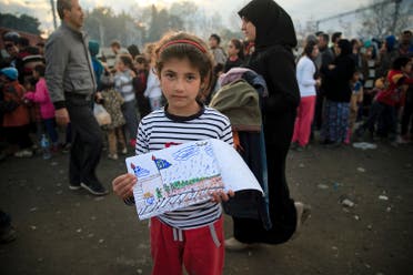 Shaharzad Hassan, 8 year-old from the Syrian city of Aleppo poses with a drawing she made as people wait in line for food rations at the northern Greek border station of Idomeni, Friday, March 11, 2016. At an overcrowded refugee camp on the Greek-Macedonian border, 8-year-old Shaharzad Hassan draws pictures of the harrowing events in her life over the past 18 months: Pictures of death in her home town of Aleppo, Syria, and her perilous journey to Europe. The title, of this drawing seen at top right reads 