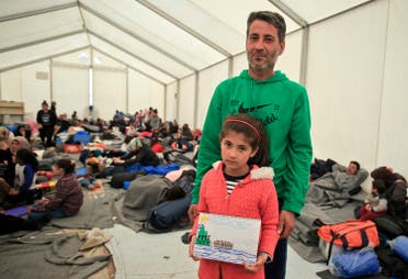 Shaharzad Hassan, 8 year-old from the Syrian city of Aleppo poses with her father Mohamed Hussein Hassan, holding a drawing she made, depicting migrants sailing in a dinghy, at the northern Greek border station of Idomeni, Friday, March 11, 2016. At an overcrowded refugee camp on the Greek-Macedonian border, 8-year-old Shaharzad Hassan draws pictures of the harrowing events in her life over the past 18 months: Pictures of death in her home town of Aleppo, Syria, and her perilous journey to Europe. The title of this drawing is 