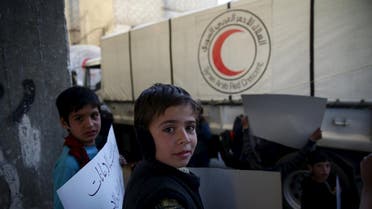 Children carry placards during an anti-government demonstration near a Red Crescent aid convoy in the rebel held besieged town of Jesreen, in the eastern Damascus suburb of Ghouta, Syria March 7, 2016. REUTERS