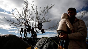 A man carrying a child walks in front of a tree with clothes drying on it at the Athens' port of Piraeus, on Saturday, March 19, 2016.  AP