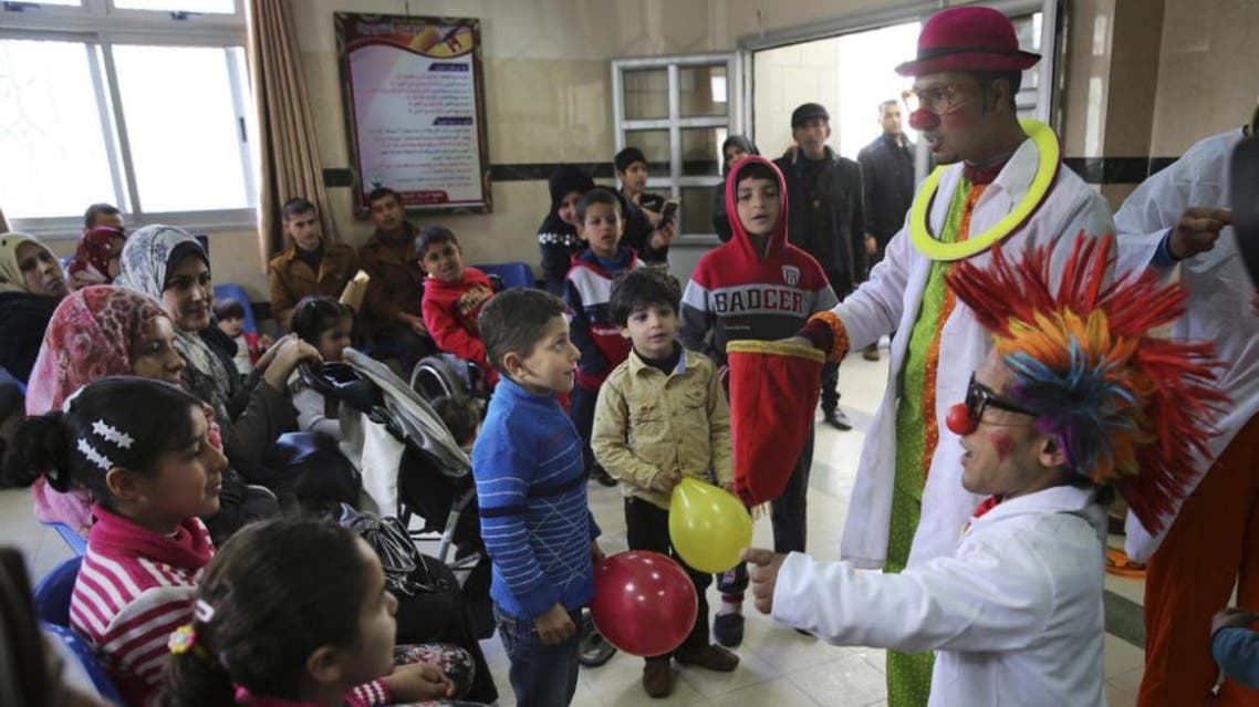 In this Thursday, March 17, 2016 photo, Palestinian clown doctors 24-year-old Majed Kaloub, top right, and 33-year-old Alaa Miqdad, right, perform for children during their visit at the waiting room at Al-Rantisi children’s hospital in Gaza City (AP)