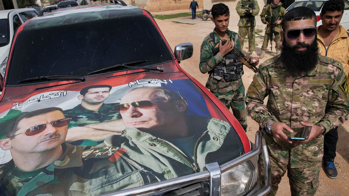 Syrian solders and Russian solders, who escort a group of journalists in the background, stand near a car covered by collage showing photos of faces of Russian President Vladimir Putin, right, Syrian President Bashar al-Assad,