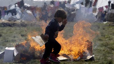 A refugee boy passes by cardboard boxes set on fire by other children, at the transit center for refugees near northern Macedonian village of Tabanovce on the border with Serbia, Monday, March 28, 2016. More than 1,000 refugees and migrants remain stranded in northern Macedonia since earlier this month, after a string of countries shut down the Balkan route which migrants used to go from Greece to central and northern Europe. (AP)