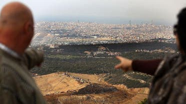 A Lebanese couple point from their balcony in the village of Baawarta at trucks unloading garbage at the Naameh landfill, south of Beirut, on March 30, 2016. (AFP)