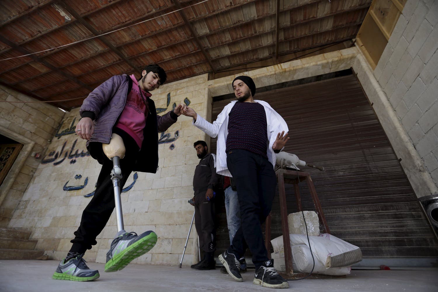 Khamis (R), 24, helps a man with an amputated leg walk using an artificial limb in the rebel-controlled area of Maaret al-Numan town in Idlib province, Syria March 20, 2016. Reuters