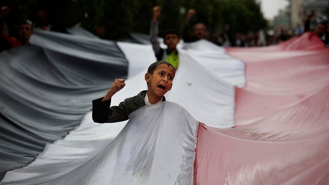 A boy chants slogans through a gap in a national flag raised by Shiite rebels, known as Houthis, during a protest against Saudi-led airstrikes in Sanaa, Yemen, Friday, April 15, 2016. (AP Photo/Hani Mohammed)