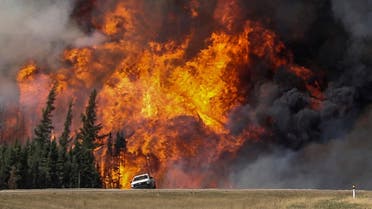 Smoke and flames from the wildfires erupt behind a car on the highway near Fort McMurray, Alberta, Canada, May 7, 2016. REUTERS