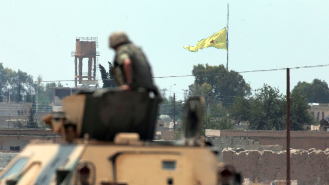 a Turkish soldier on an armoured personnel carrier watches as in the background a flag of the Kurdish People's Protection Units, or YPG, is raised over the city of Tal Abyad, Syria, Tuesday, June 16, 2015. ap