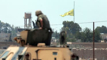 a Turkish soldier on an armoured personnel carrier watches as in the background a flag of the Kurdish People's Protection Units, or YPG, is raised over the city of Tal Abyad, Syria, Tuesday, June 16, 2015. ap