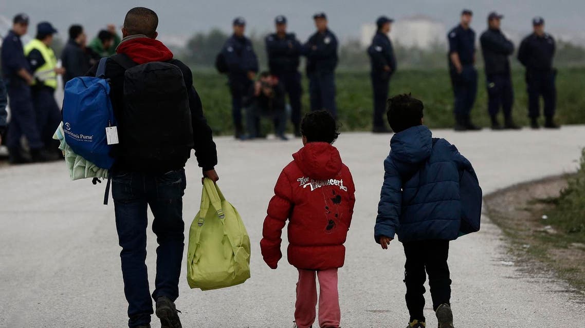 Refugees carry their belongings in front of riot policemen during a police operation at a refugee camp at the border between Greece and Macedonia, near the village of Idomeni, Greece, 24 May 2016. REUTERS