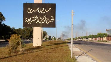A sign which reads in Arabic, "The city of Sirte, under the shadow of Sharia" is seen as smoke rises in the background. (Reuters)