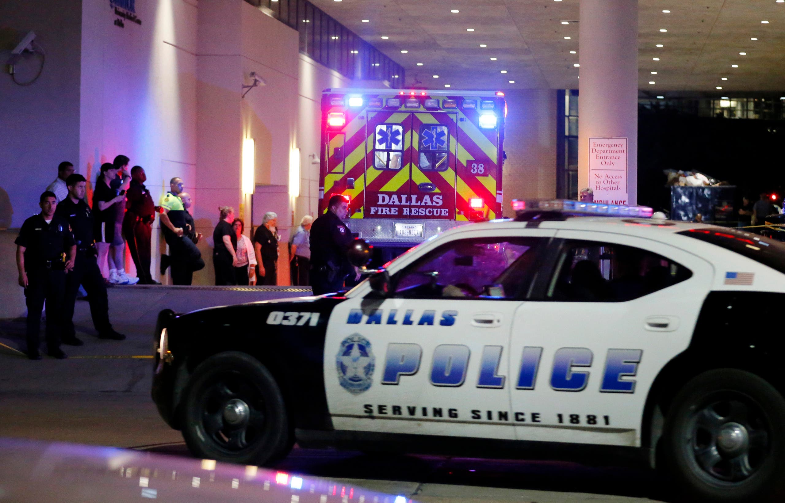 A Dallas police vehicle follows behind an ambulance carrying a patient to the emergency department at Baylor University Medical Center, as police and others stand near the emergency entrance early Friday, July 8, 2016, in Dallas. (AP)