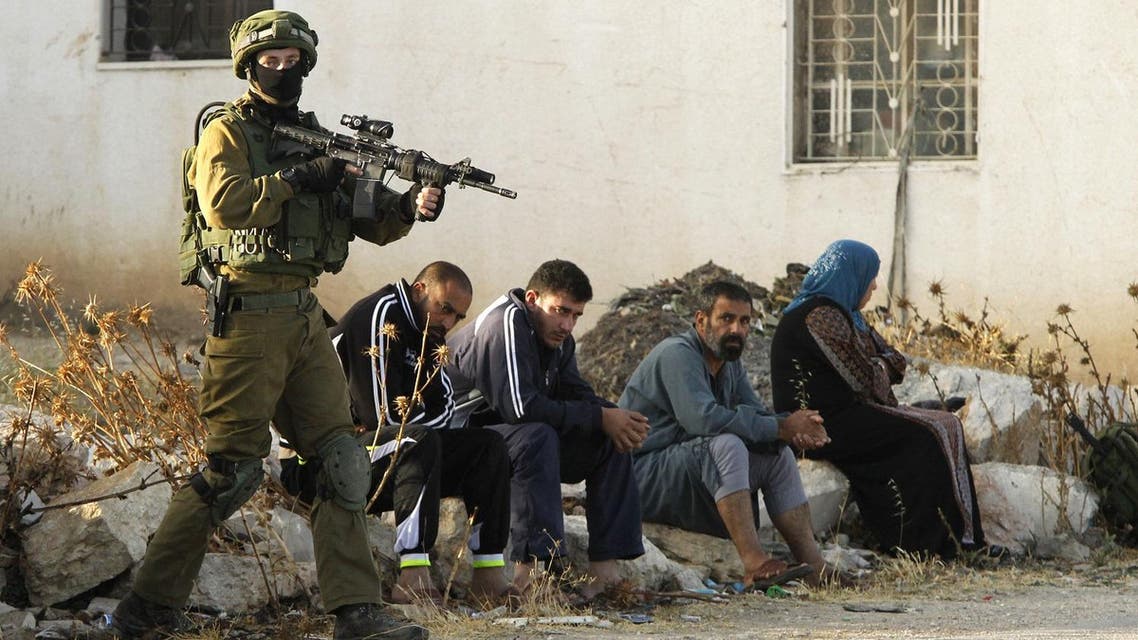 An Israeli soldier keeps watch as Palestinians sit nearby after the army entered the village of Yatta in the occupied West Bank. (AFP)