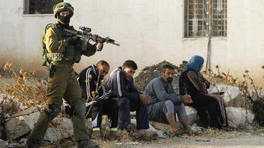 An Israeli soldier keeps watch as Palestinians sit nearby after the army entered the village of Yatta in the occupied West Bank. (AFP)