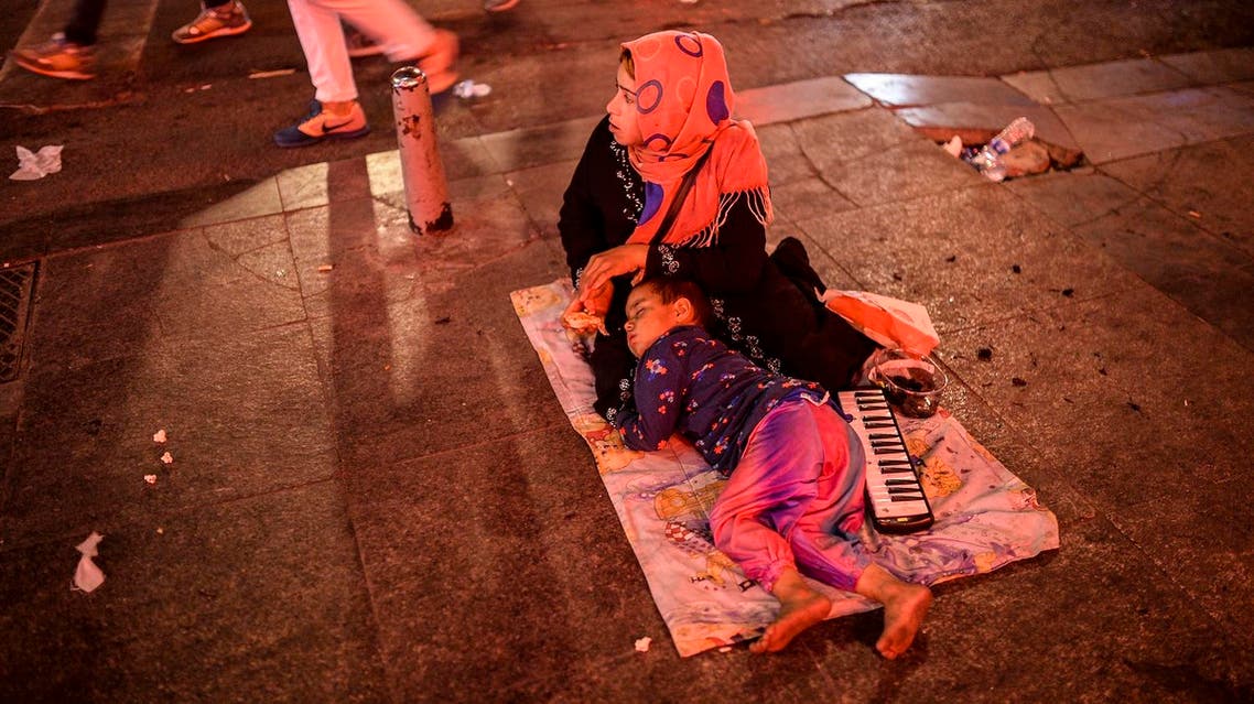 A Syrian refugee woman sits as a child sleeps near her early in the morning on Taksim Square, Istanbul. (AFP)