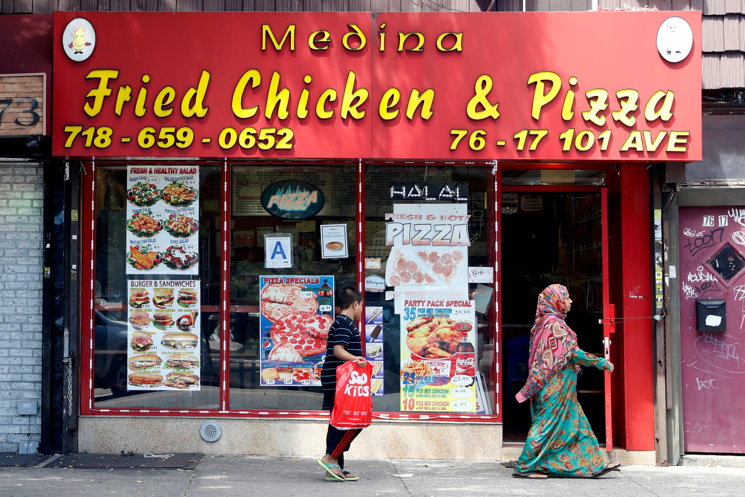 In this Wednesday, Aug. 17, 2016, photo a Muslim woman and her son walk past a Halal restaurant in the Ozone Park neighborhood of the Queens borough of New York. The shooting of an imam and his assistant near their New York mosque has unnerved Muslim residents of the Ozone Park section of Queens. (AP)