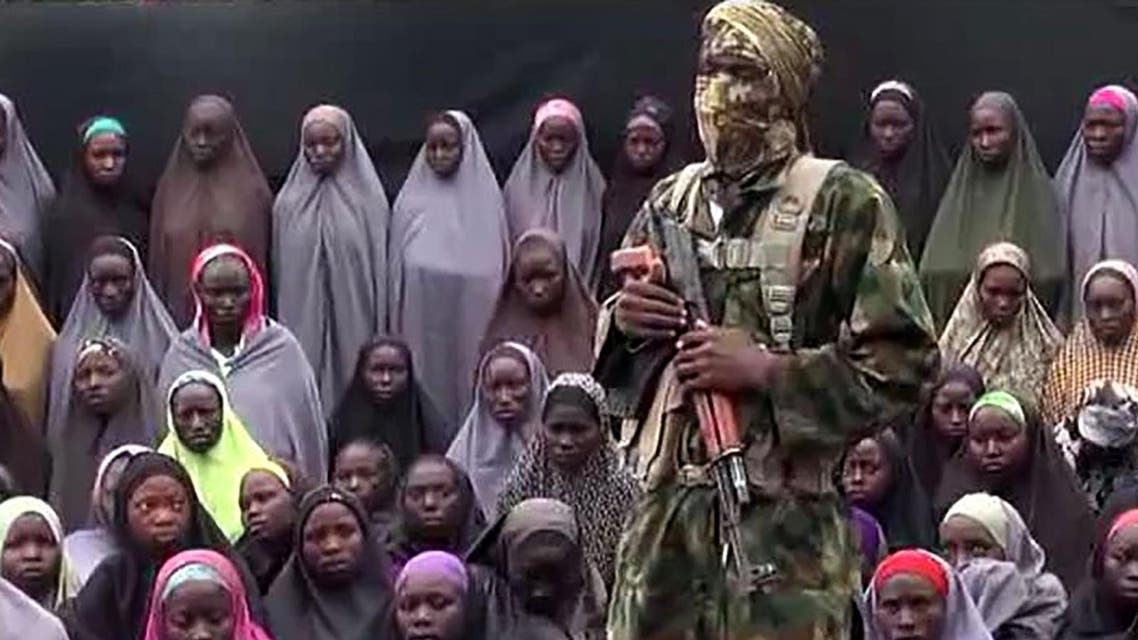 This video grab image created on August 14, 2016 taken from a video released on youtube purportedly by Islamist group Boko Haram showing what is claimed to be one of the groups fighters at an undisclosed location standing in front of girls allegedly kidnapped from Chibok in April 2014. AFP