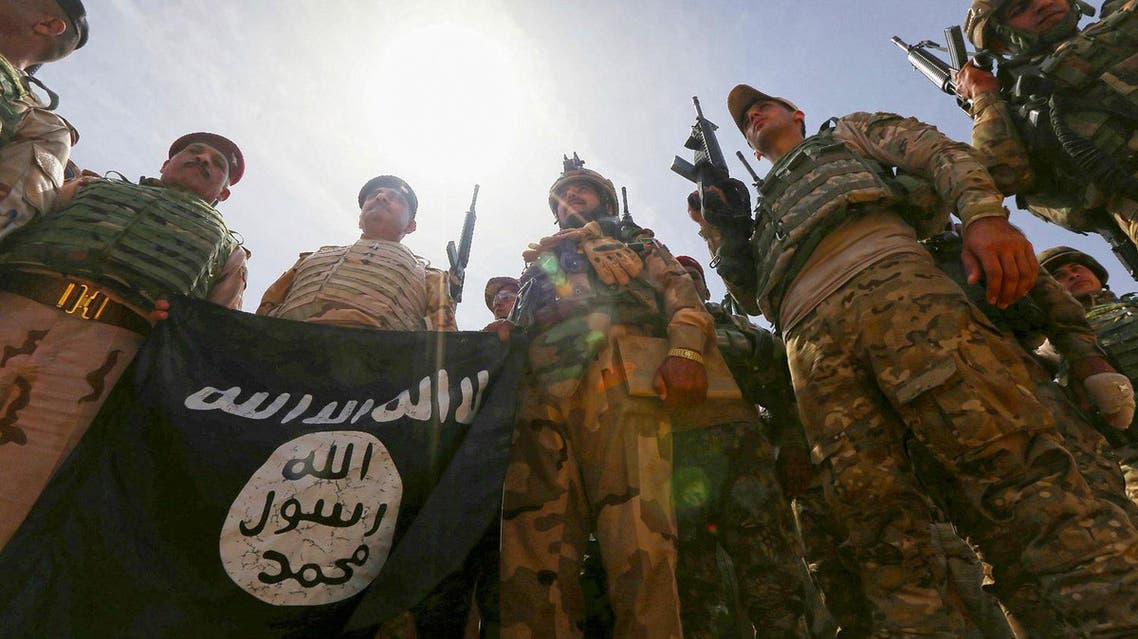 Iraqi soldiers hold a flag that they seized from ISIS as they hold a position near the frontline on April 9 in the town of Kharbardan, located 10 kms south of Qayyarah. (File photo: AFP)