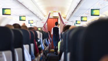 Interior of airplane with passengers on seats and stewardess walking the aisle. shutterstock