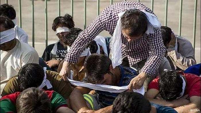 شرطي إيران يقوم بتعصيب أعين المعتقلين الأفغان