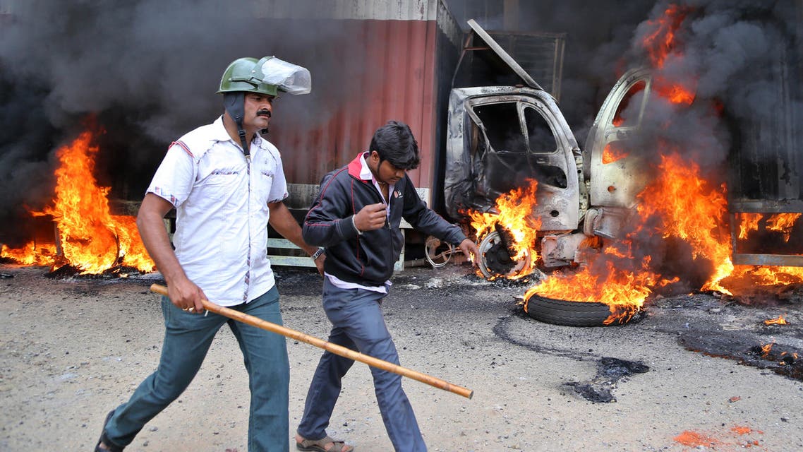 An Indian police officer detains a youth as they walk past burning trucks that belong to the neighboring Tamil Nadu state set ablaze by angry mobs in Bangalore, Karnataka state, India, Monday, Sept. 12, 2016. (AP)