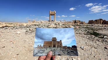 A general view taken on March 31, 2016 shows a photographer holding his picture of the Temple of Bel taken on March 14, 2014 in front of the remains of the historic temple after it was destroyed by Islamic State (IS) group jihadists in September 2015 in the ancient Syrian city of Palmyra. AFP