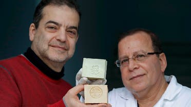 Franco-Syrian Samir Constantini (L), CEO of Alepia brand, and Syrian master soapmaker Hassan Harastani, who fled Syria and decided to produce Aleppo soap on French soil, pose December 22, 2016, holding bars of soap at the company's factory in Santeny, near Paris. Picture December 22, 2016. (Reuters)