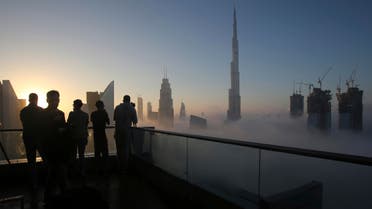 Photographers take pictures as the sun rises over the city skyline with the Burj Khalifa, world's tallest building at the backdrop, seen from a balcony on the 42nd floor of a hotel on a foggy day in Dubai, on Dec. 31, 2016. (AP). 