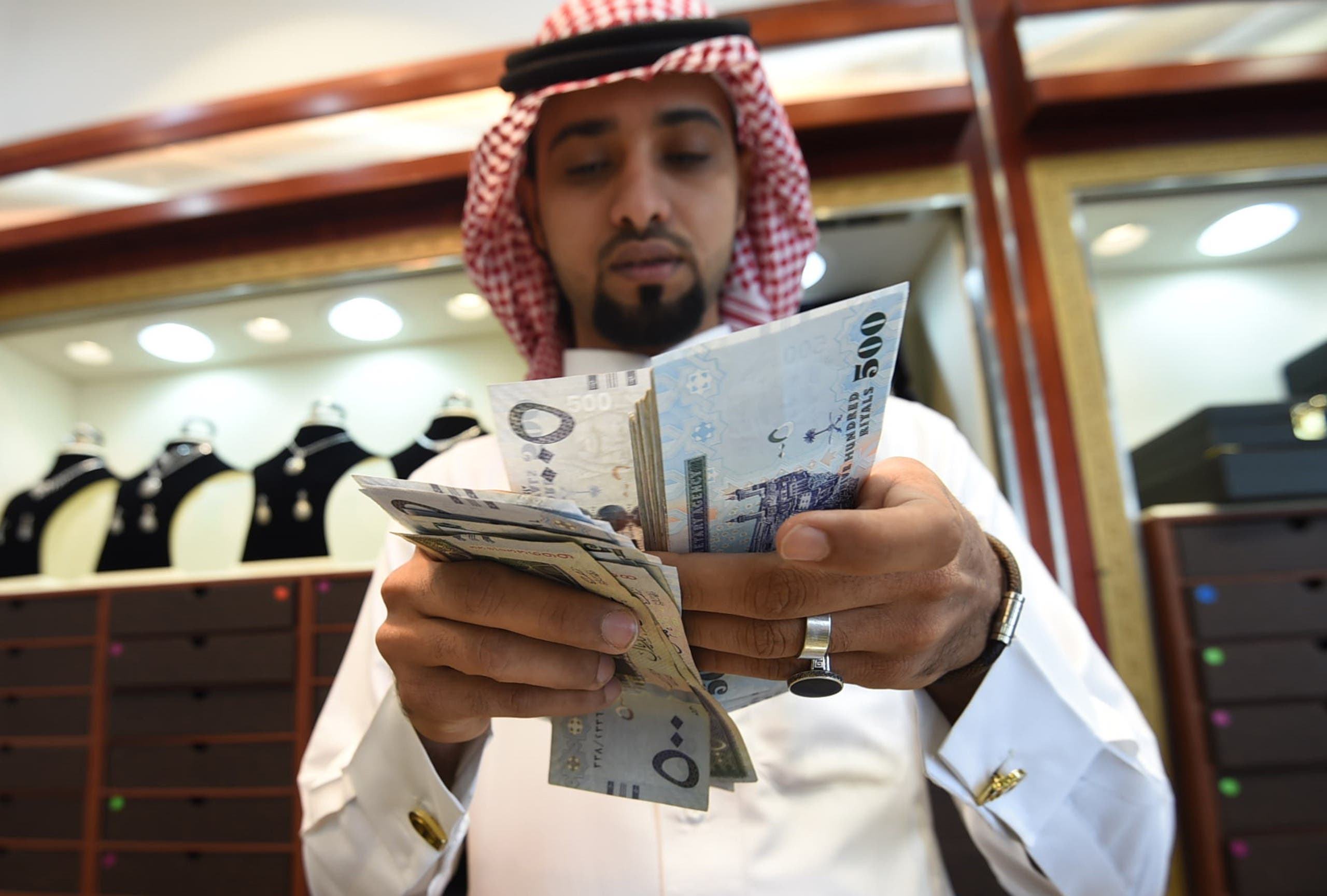 A Saudi man counts banknotes at his jewelry shop at Tiba market in Riyadh, on October 3, 2016. Since 2014 global oil prices have collapsed by more than half, leaving Saudi Arabia with a record deficit last year. The shortfall in the kingdom's main revenue source had already led to unprecedented subsidy cuts and a slowdown in government projects as the administration tries to diversify the economy. FAYEZ NURELDINE / AFP