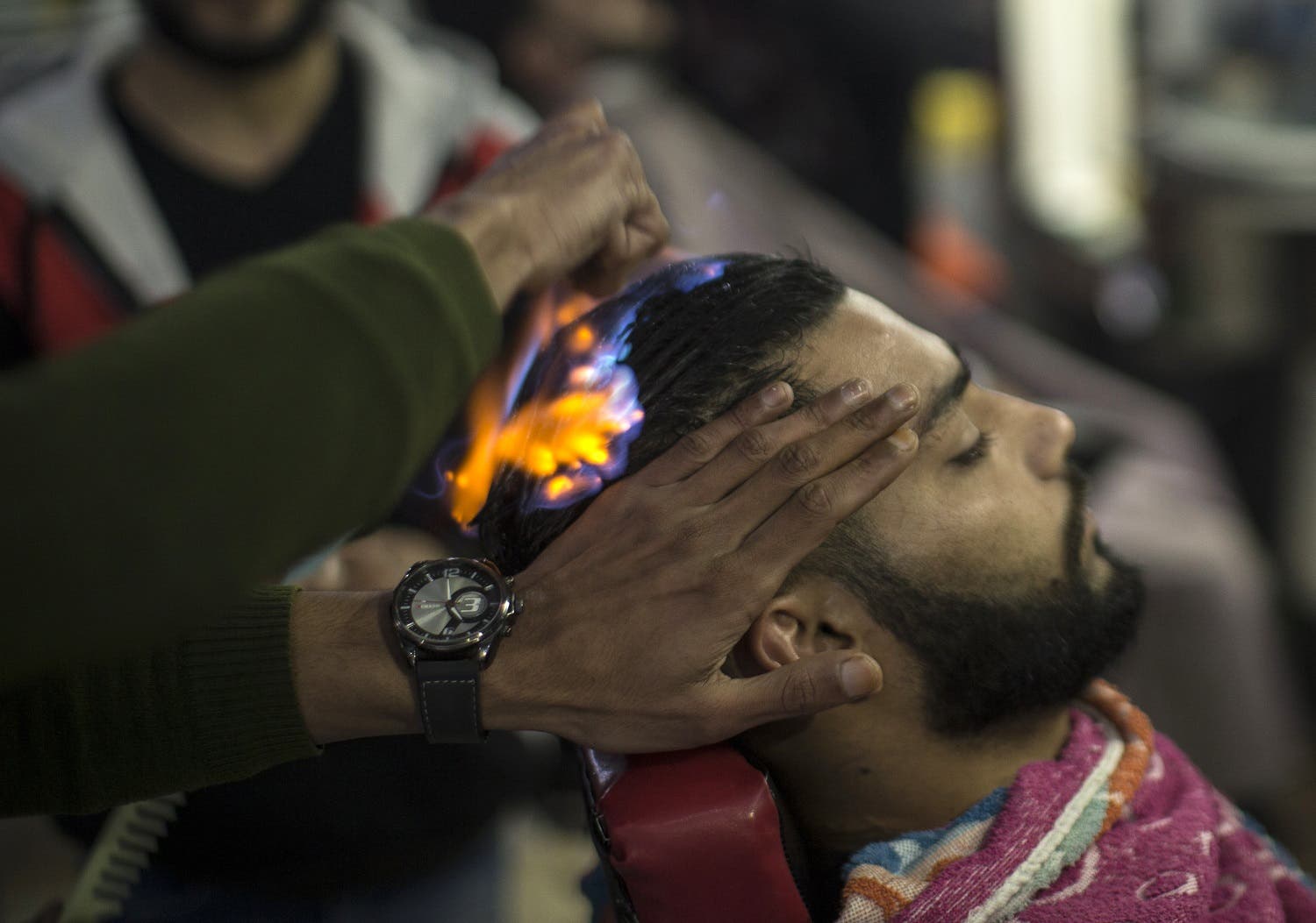 A client sits in a hair salon as barber Ramadan Edwan performs a technique that utilises fire to straighten his hair, in the Rafah refugee camp, in the southern Gaza Strip on February 1, 2017. MAHMUD HAMS / AFP