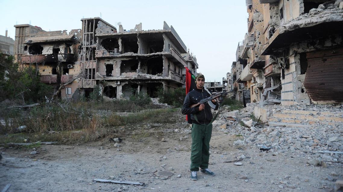 A civilian fighter holding the Libyan flag stands in front of damaged buildings in Benghazi, Libya (File Photo: AP/Mohammed el-Shaiky)