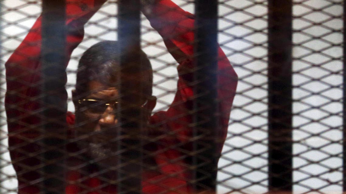 Deposed President Mohamed Mursi greets his lawyers and people from behind bars at a court wearing the red uniform of a prisoner sentenced to death, during his court appearance with Muslim Brotherhood members on the outskirts of Cairo, Egypt, June 21, 2015. (Reuters)