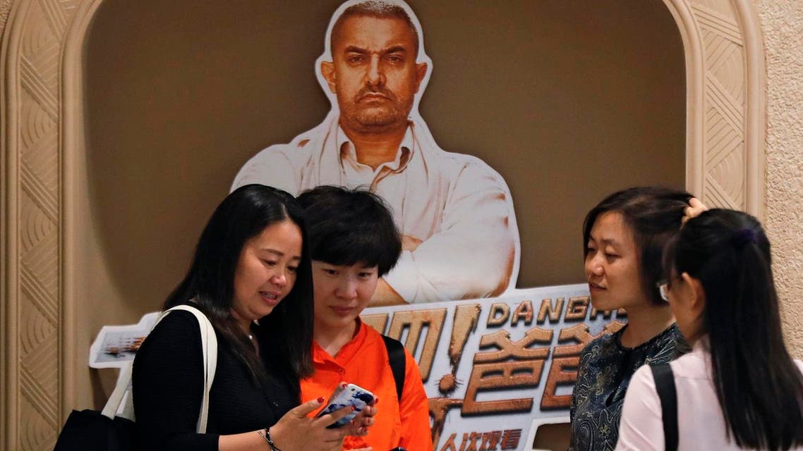 In this May 22, 2017 photo, a Chinese woman browses a photo which she took with her friends with a poster of blockbuster film “Dangal,” back, at a cinema in Beijing. (AP)