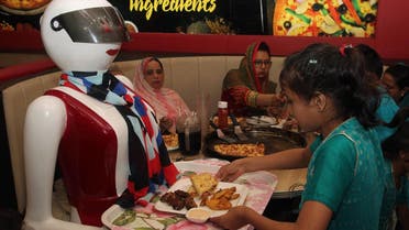 In this photograph taken on July 4, 2017, a young customer picks up food from a tray carried by a robot waitress at a pizza restaurant in Multan. (AFP)