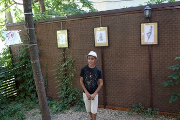 Farhad Nouri observes his drawings on display at an art exhibition in Belgrade, Serbia, Wednesday, Aug. 9, 2017. Nouri, a migrant boy from Afghanistan, has been nicknamed Little Picasso for artistic talent, and is using his first ever exhibition to help another little boy in need, a Serbian boy recovering from brain tumor surgery. (AP Photo/Marko Drobnjakovic)