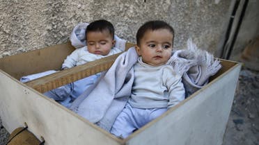 Five-month-old twins Farah and Marah wait for their parents to receive milk distributions from a medical center in the Hamoria area, in the eastern Damascus suburb of Ghouta, Syria, October 25, 2017. (Reuters)