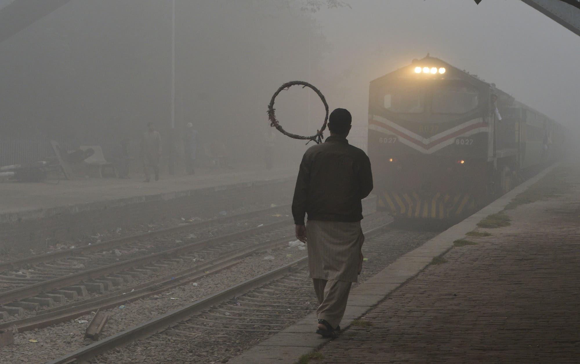 A Pakistani railway worker walks on the platform while a train arrives at a station in heavy smog in Lahore on November 6, 2017. (AFP)