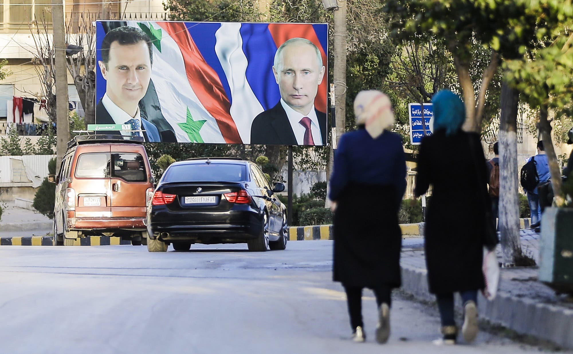 A picture taken on March 9, 2017 in Aleppo shows Syrians walking past a giant poster of Bashar al-Assad and Vladimir Putin. (AFP)