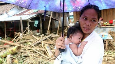 A woman stands with her baby in front of damaged houses and fallen trees in Barangay San Mateo Borongan in eastern Samar. (AFP)