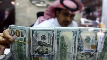 A Saudi money changer, pictured through a glass, arranges U.S banknotes at a currency exchange shop in Riyadh. (Reuters)