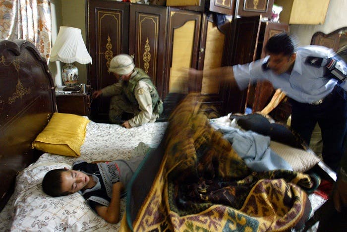 A U.S. soldier and Iraqi policeman search a room as an Iraqi child sleeps on the bed during a joint raid. (Reuters)