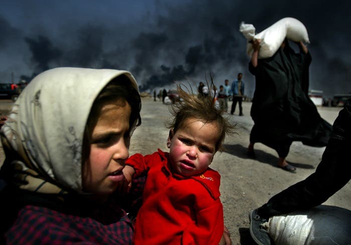 An Iraqi girl holds her sister as she waits for her mother (R) to bring over food bought in Basra, March 29, 2003. (Reuters)