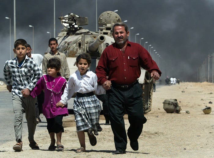 A family flees past a destroyed Iraqi T-55 tank after a mortar attack on British Army positions in the southern city of Basra, March 28, 2003. (Reuters)