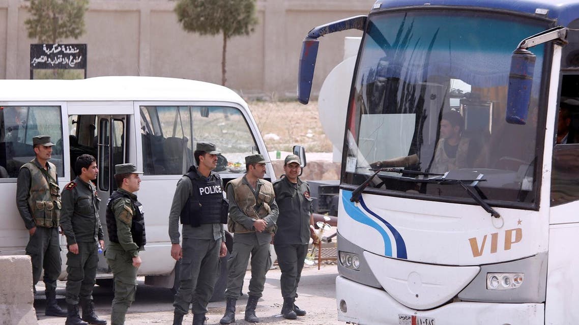 Syrian Army soldiers stand next to buses that carry rebels and their families who left Douma, at the entrance of the Wafideen camp in Damascus, Syria, ON April 12, 2018. (Reuters)