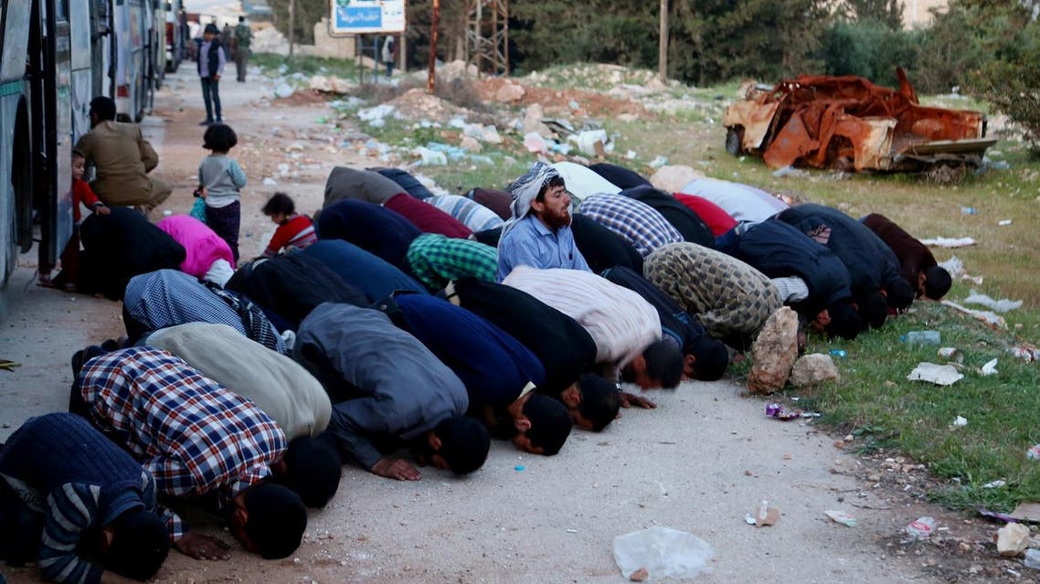 Syrian men pray as buses with Jaish al-Islam fighters and their families on board arrive from their former rebel bastion of Douma in Eastern Ghouta at the Abu al-Zindeen checkpoint, on April 14, 2018. (AFP)